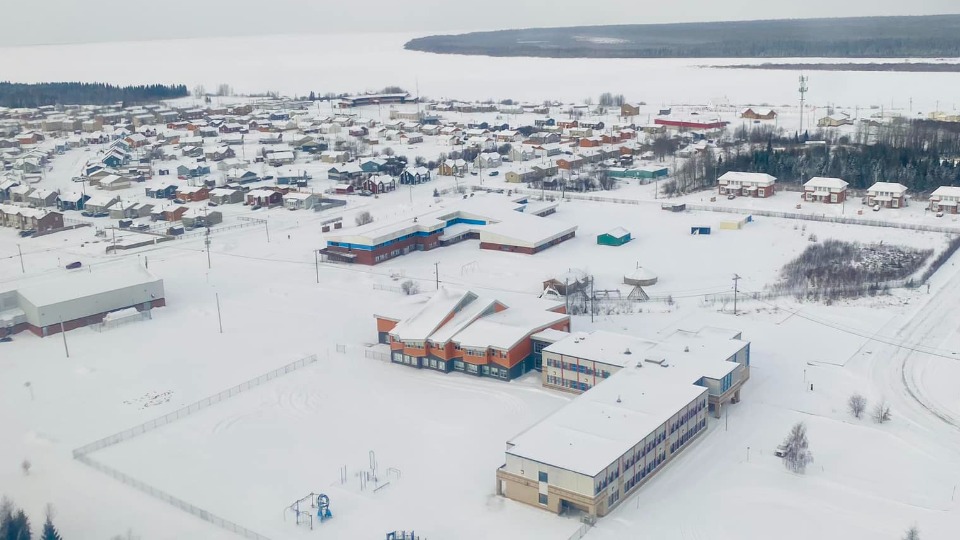 La communauté crie de Waskaganaish, vue aérienne d'une école, et derrière se trouves des dizaines de maisons enneigée et la rivière Rupert .