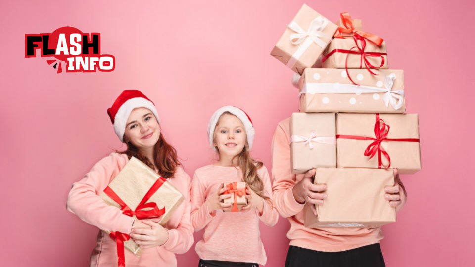 Trois personnes coiffées de bonnets rouges et blancs posent avec des tas de cadeaux emballés.