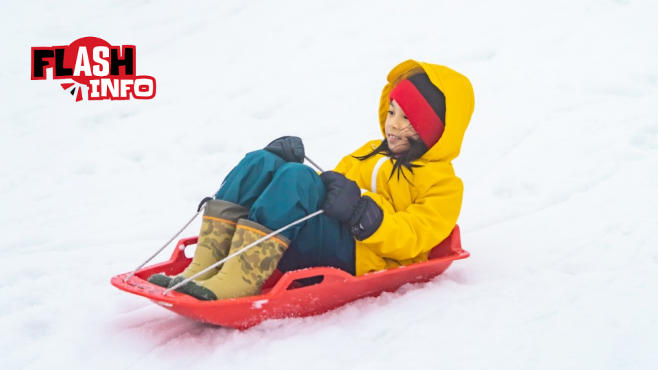 Une enfant glisse en traîneau sur une pente enneigée.
