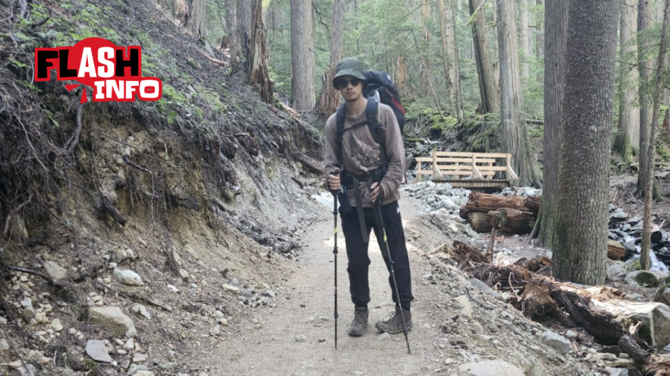 Un randonneur pose dans un sentier, équipé d’un sac à dos, de verres fumés et d’un chapeau.