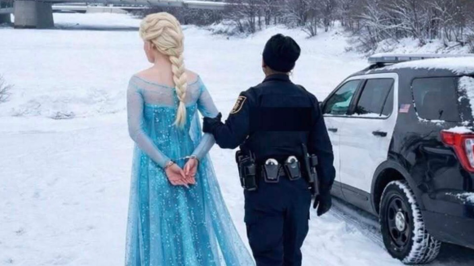 Dehors, dans la neige, une policière accompagne la reine des neiges qui a les mains menottées. 