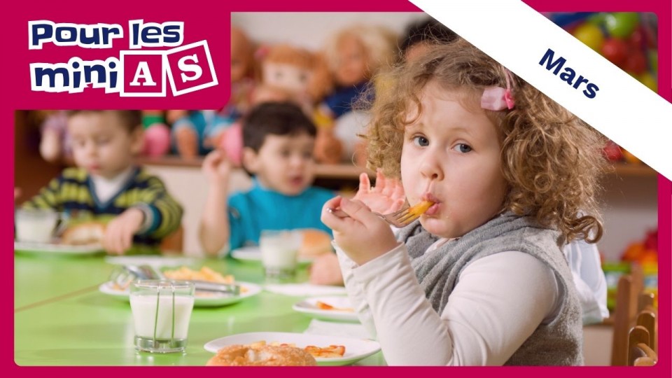 Une fillette qui mange, assise sur une petite table. 