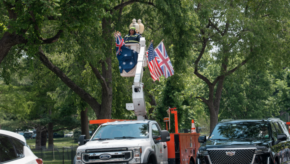 On voit une dame dans la cage qui monte et qui descend d'un camion. Elle est en train d'enlever un drapeau de l'Australie. 
