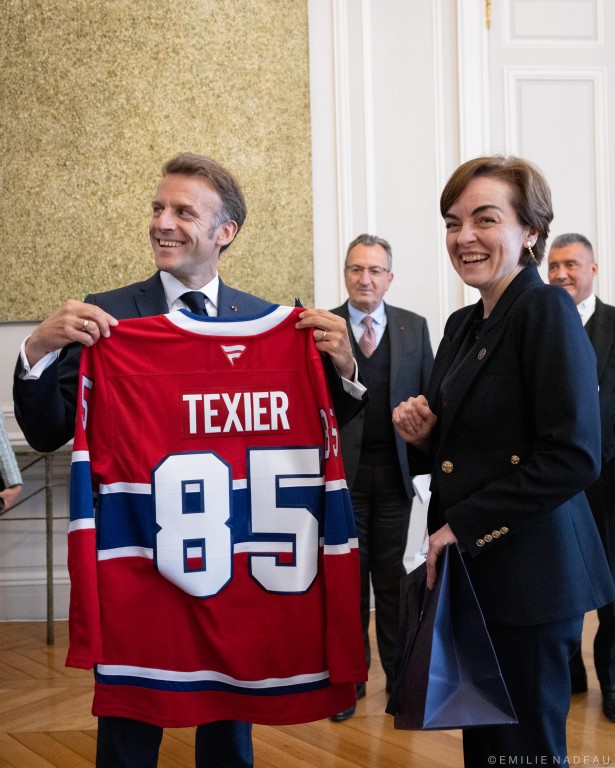 On voit le président français, Emmanuel Macron, qui sourit en tenant un chandail du Canadien de Montréal. C'est celui du numéro 85, qui porte le nom Texier. À côté du président, il y a la première ministre du Québec, Christine Fréchette, qui rit. 